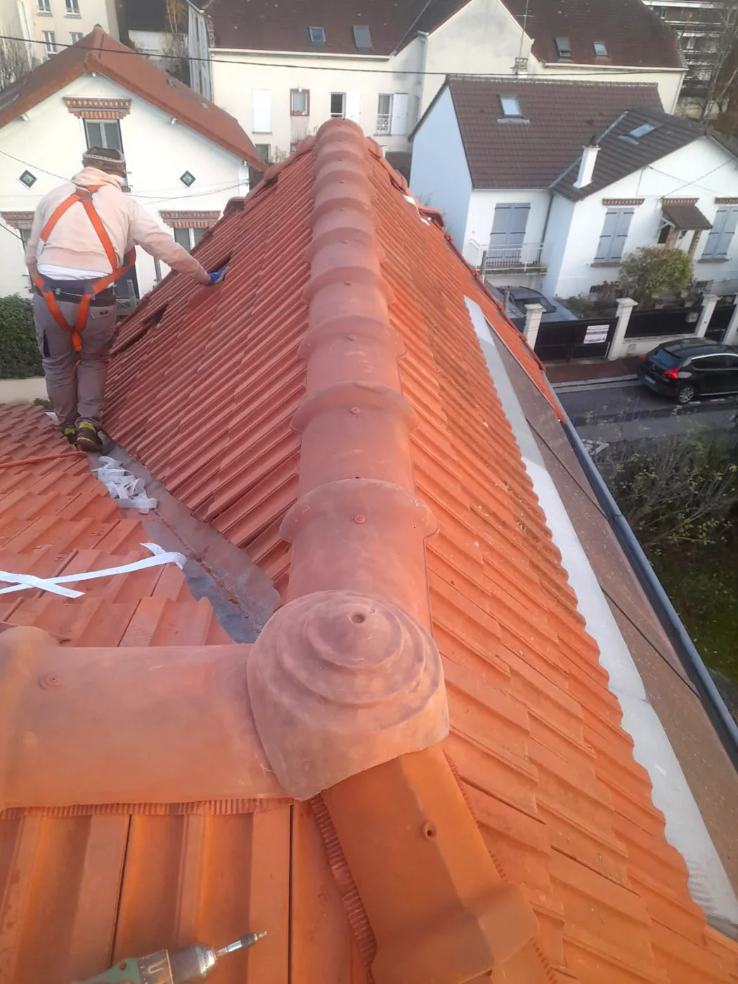 Un couvreur harnaché progresse le long du faîtage d'une toiture en tuiles