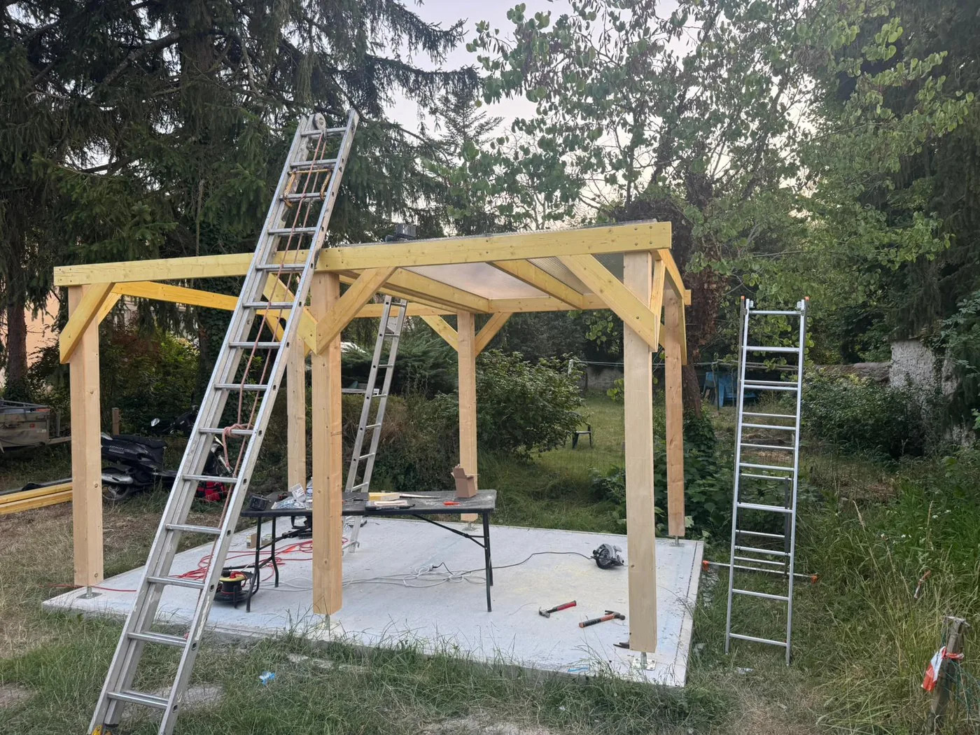 Montage de la charpente d'une pergola, deux échelles en appui